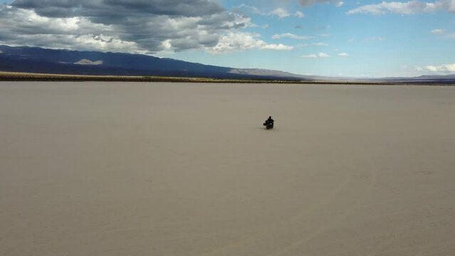 Motorcyclist rides across sand flat Pampe del leoncito in Argentina
