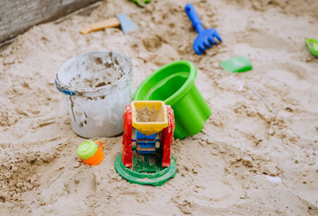 Multi-colored plastic children's toys in a sandbox with sand on a playground for children to play. Closeup photo, childhood concept.