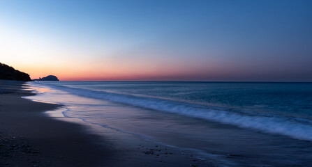 Sunrise at the Yanışlı beach on the background of  reddish sky and waves come ashore of the Mediterranean Sea at the long exposure