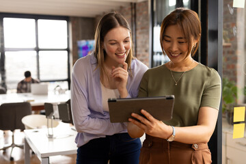 A mature Asian female professional and young Caucasian female colleague holding a tablet in a modern