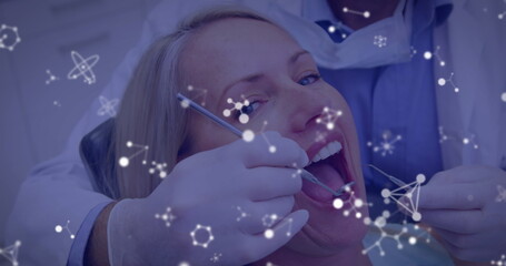 Image of molecules flowing over male dentist with face mask treating female patient in dentist chair