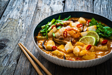 Tom Yum - Thai soup with halibut nuggets and rice noodles on wooden table
 - obrazy, fototapety, plakaty