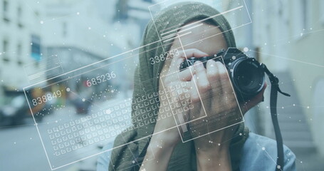 Image of financial data processing over biracial woman in hijab taking photos