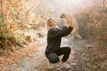 Smiling blonde woman holding small dog outdoor with sunshine