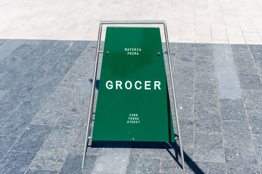 stylish contemporary sidewalk sign board outside Stock TC Grocer, a grocery and take out joint, located on the ground floor of 2388 Yonge Street in Toronto, Canada