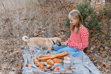 Teenage girl with dog sitting on a plaid with drink and bakery on a picnic