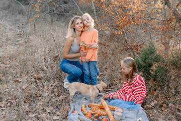 Blonde mother with her cute girls and dog on a picnic outdoor in park