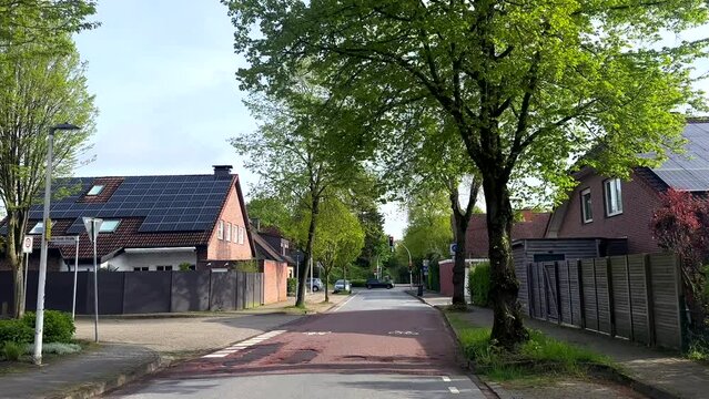 POV on street of german small town with modern solar panels on homes in spring season. Housing area with single family houses in red bricks. Bicycle lane in suburb.