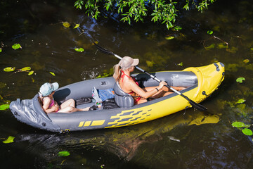 A young mother with daughter is kayaking on the river on a summer day.
