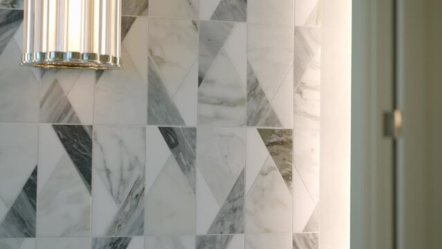 Luxurious interior of bathroom featuring marble wall with striking geometric pattern. Ambient light from modern lighting fixture accentuating texture of stone and elegant design