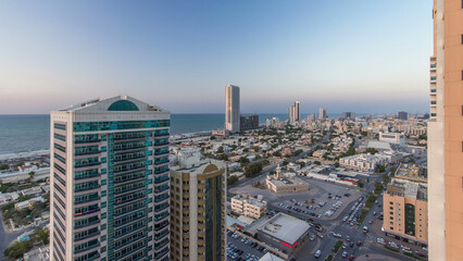 Cityscape with towers in Ajman from rooftop day to night timelapse. United Arab Emirates.