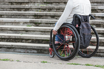 Woman in a wheelchair stopping and waiting at the bottom of inacessible street staircase, unable to...
