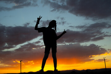 Girl poses with a peace sign against the backdrop of the sunset sky