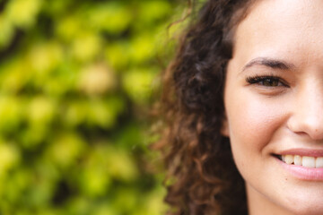 A young Caucasian woman with curly hair, smiling outdoors, copy space