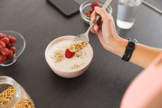 A young Caucasian woman wearing fitness tracker eating breakfast at home