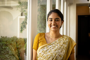 Indian young woman wearing yellow sari, smiling at home near window