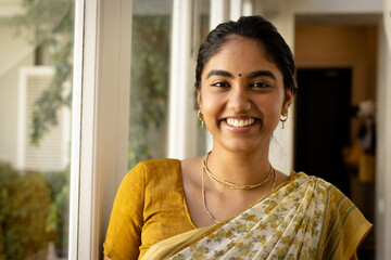 Indian young woman wearing traditional yellow saree, smiling at home