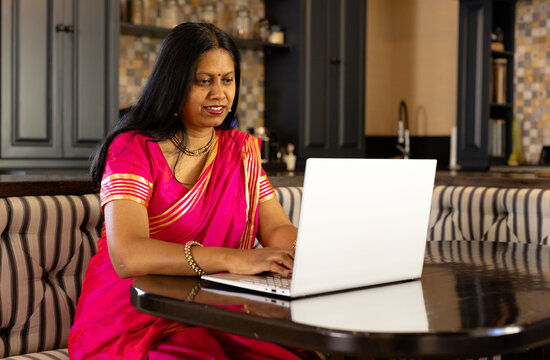 Indian woman in bright pink saree using laptop at home