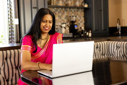 Fototapeta Indian woman wearing pink sari working on laptop at home