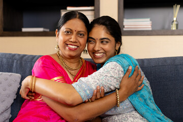 Indian mother and teenage daughter, wearing traditional clothes, hugging at home