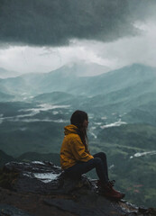 Girl in a jacket sitting on the edge of a mountain while it is raining