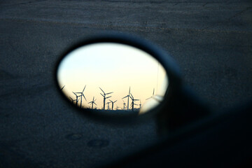 Wind turbines reflected in a car's rearview mirror at dusk.