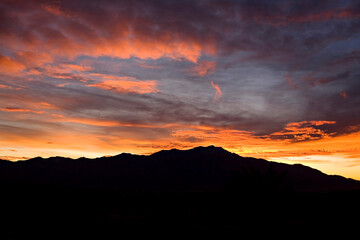 Fiery sunset silhouettes mountain range under a vibrant twilight sky.
