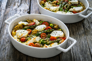 Obraz premium Bread casserole with green asparagus, goat cheese, tomatoes and eggs on wooden table 