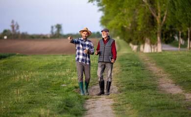 Two farmers walking and discussing on dirt road in field