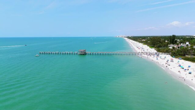 Drone view of Naples, Florida with wide stretch of white sandy beach and calm turquoise waters of ocean extending to horizon and reflecting clear blue sky above