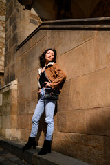 Fashionable woman in jacket and jeans by stone wall.