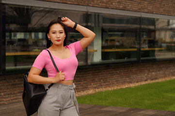 Woman in pink top and grey trousers by modern building.