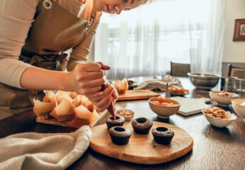 Woman skillfully decorates cupcakes on a wooden board, surrounded by baking supplies and kitchen...