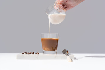 Vertiendo leche en un vaso transparente de café sobre mármol y fondo gris	