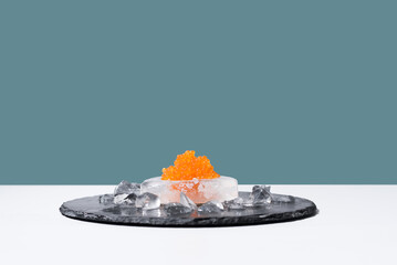 Caviar de salmón sobre hielo en un plato de pizarra. Comida gourmet sobre fondo verde	