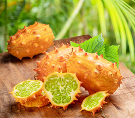 Kiwano fruit with kiwano slices on wooden background. Blurred tropical nature background.