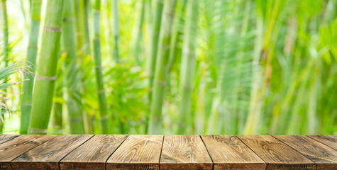 Empty wooden board or table top and blurred green bamboo culms. Place for your product display.