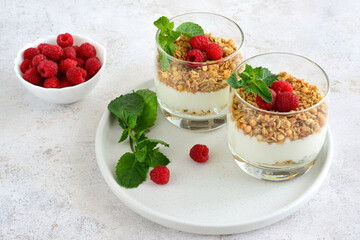 two glasses of oatmeal, yogurt and raspberries with green mint leaves   