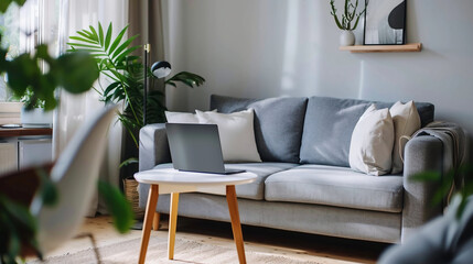 Interior of light living room with grey sofa and laptop on table