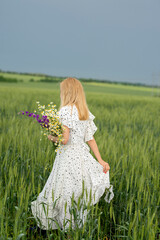 cute feminine blonde girl with wet hair and a bouquet of wildflowers in the field. View from the...