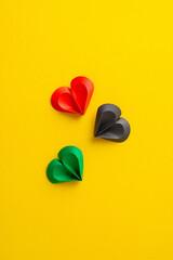 Three paper hearts in red, black, and green colors arranged on a vivid yellow vertical surface,...