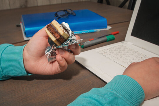 A child eats a cake while using a computer. Unhealthy diet in children - Powered by Adobe