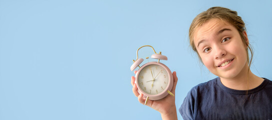 A girl is holding a pink alarm clock and smiling. The clock is set to the time of 7.30. Copy space....