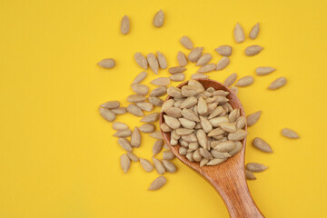 Photograph of  peeled sunflower seeds without shells in a wooden spoon on bright yellow background....