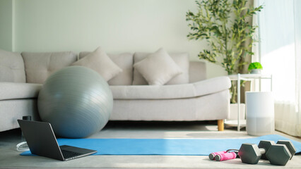 Laptop and exercise equipments on mat on floor for training at home.