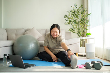 Overweight woman exercising in the living room watching online tutorial on laptop.