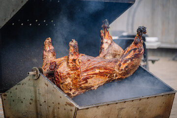 Dobele, Latvia - August 18, 2023 - A whole pig being roasted on a large barbecue grill with a...