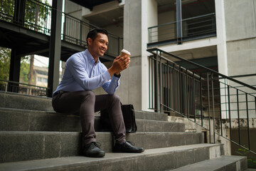 Smiling businessman enjoying morning coffee while sitting on stairs of office building