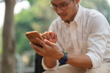 Millennial businessman in eyeglasses using mobile phone in the city park