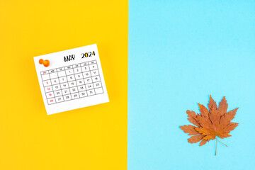 Top view of a May 2024 calendar and autumn foliage on a yellow and blue background. Empty space provided for text.